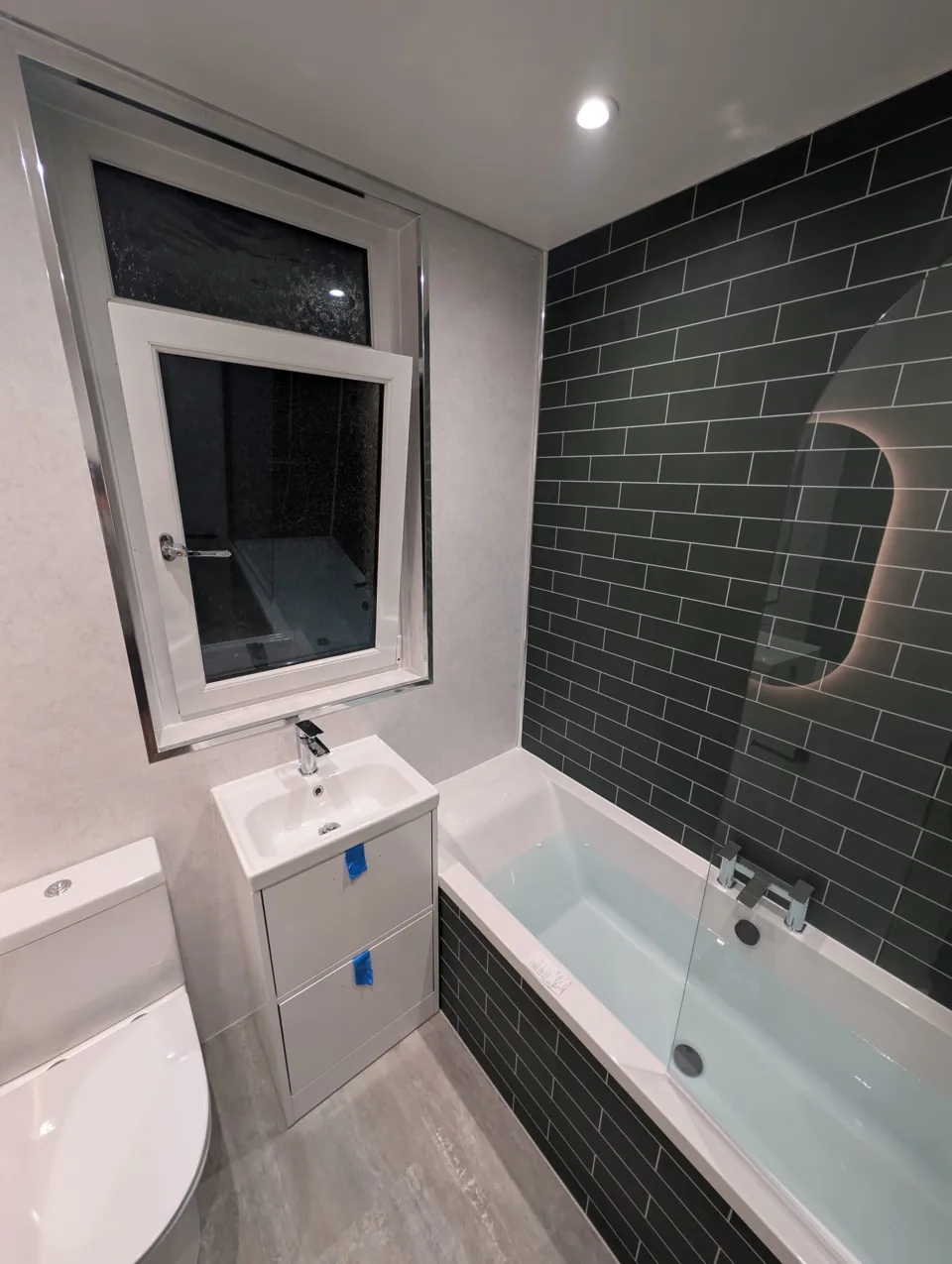 Fitted bath with green tiles and white bathroom furniture