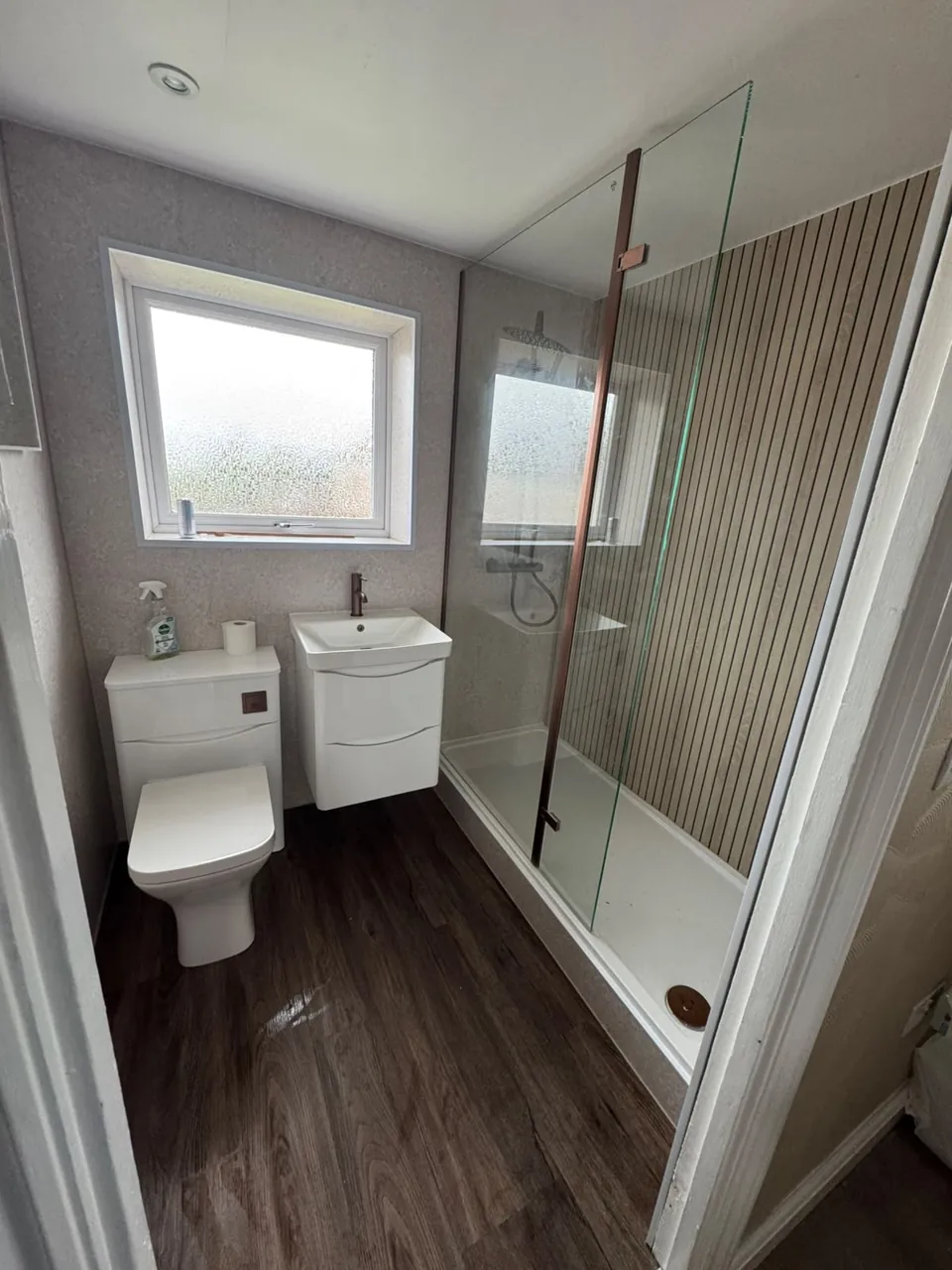 Glass shower enclosure beside a wood-effect feature wall